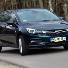 Ciemnozielona Astra K 1.6 CDTI w ruchu, z widocznym kierowcą za kierownicą, na tle lasu.