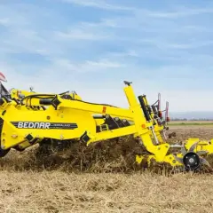 Czerwony traktor z żółtym agregatem uprawowym Bednar Terraland pracuje na polu.