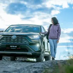 Kobieta obok Toyoty RAV4, jednego z najmniej awaryjnych crossoverów, na tle nieba z chmurami.