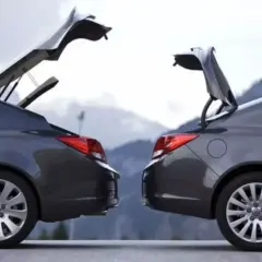 Dwa ciemnoszare sedany z otwartymi bagażnikami, przypominające kształtem hatchback. Góry w tle.