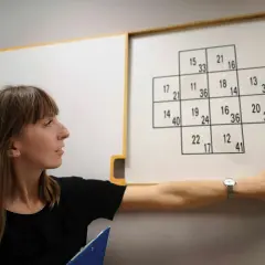 Kobieta podczas testów psychologicznych dla kierowców, wskazująca na tablicę z liczbami.
