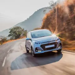 Srebrny Hyundai przemierza krętą drogę w słoneczny dzień. Ten Hyundai z jakiego kraju pochodzi? Z Korei Południowej, gdzie powstała ta marka.