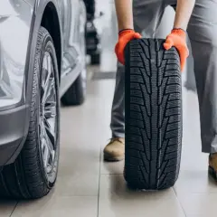 Mechanik w pomarańczowych rękawiczkach trzyma nowe opony letnie obok samochodu. Czas na test opon letnich!