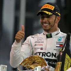 Lewis Hamilton, jeden z najlepsi kierowcy f1, świętuje zwycięstwo z pucharem i szampanem, pokazując kciuk w górę.