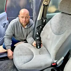 Mężczyzna z butelką środka do mycia tapicerki samochodowej przygotowuje się do odświeżenia wnętrza auta.