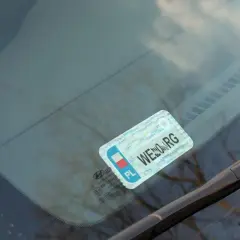 Naklejki na samochód, w tym obowiązkowe naklejki z numerem rejestracyjnym, umieszczone na przedniej szybie.