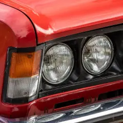 Czerwone auto z włoch, z podwójnymi okrągłymi reflektorami i pomarańczowym kierunkowskazem.