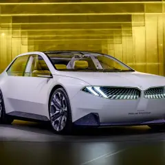 Biały koncept BMW Neue Klasse z futurystycznymi światłami i żółtym wnętrzem, prezentowany na tle złotej, lśniącej ściany.