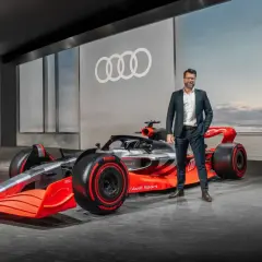 Mężczyzna w garniturze obok futurystycznego bolidu Audi F1 2026.