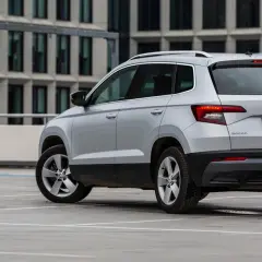 Srebrny Skoda Karoq, jeden z najmniej awaryjnych aut segmentu B, parkuje przed nowoczesnym budynkiem.