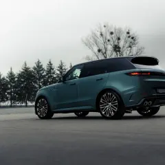 Elegancki, zielony Range Rover, jeden z prestiżowych angielskich marek samochodów, parkuje na tle drzew.