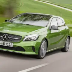 Zielony Mercedes klasy C pędzi po krętej drodze wśród zielonych pól.