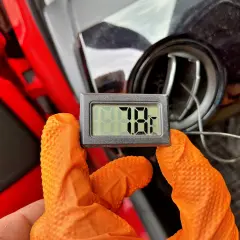 Rękawiczki w kolorze pomarańczowym trzymają termometr pokazujący 78°F. To część samodzielnego nabijania klimatyzacji.