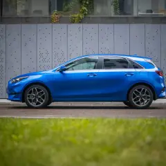 Niebieski hatchback z dynamiczną linią nadwozia, przypominającą coupe, zaparkowany przy nowoczesnej, szarej ścianie.