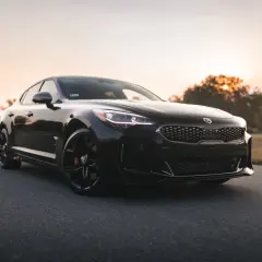 Czarna Kia Stinger, sportowy samochód z Korei Południowej, zaparkowana na pustej drodze o zachodzie słońca.