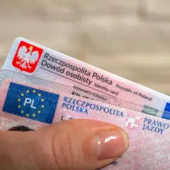 Dłoń trzyma polski dowód osobisty i prawo jazdy. Czy prawo jazdy bezterminowe trzeba wymienić? Sprawdź przepisy!