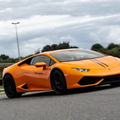 Pomarańczowe Lamborghini z czarnymi pasami na masce podczas szybkiego przejazdu po torze wyścigowym.