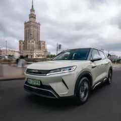 Biały SUV marki BYD, jeden z chińskich marek aut, jedzie ulicą Warszawy. W tle Pałac Kultury i Nauki.