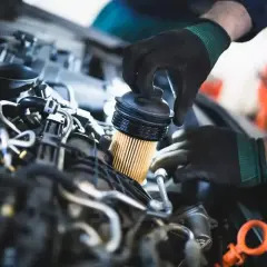 Mechanik w czarnych rękawiczkach wymienia filtr paliwa w silniku diesla.