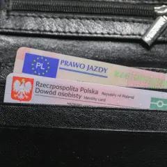 Czarny portfel z polskim dowodem osobistym i prawem jazdy. Na dokumencie prawa jazdy widnieje napis "PRAWO JAZDY" oraz symbol PL.