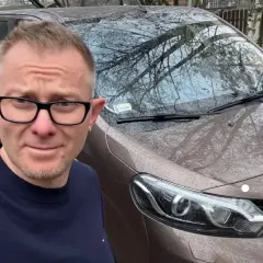 Mężczyzna w okularach przed brązowym autem, zastanawia się, jak szybko sprzedać auto.