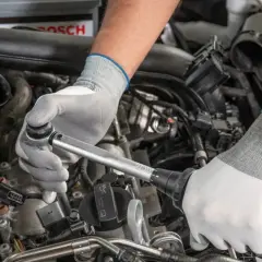 Mechanik w białych rękawiczkach dokonuje precyzyjnej wymiany świec w silniku samochodu, używając klucza dynamometrycznego.