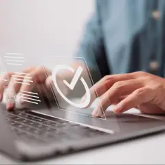 Ręce na klawiaturze laptopa, nad nią wirtualny interfejs z ikoną potwierdzenia. Proces uzyskiwania świadectwa zgodności pojazdu.