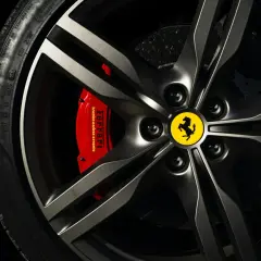 Logo samochodu ze skrzydłami na feldze Ferrari. Czerwony zacisk hamulcowy z napisem "Ferrari".