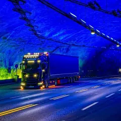 Ciężarówka jedzie przez najdłuższy tunel drogowy na świecie, oświetlony niebieskim i zielonym światłem.