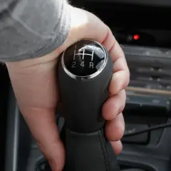 Dłoń chwyta lewarek zmiany biegów, ustawiając go na wsteczny w automacie.