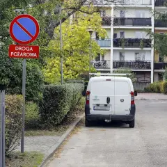 Znak zakazu postoju na drodze pożarowej. Biały bus stoi na poboczu, gdzie nie można parkować.