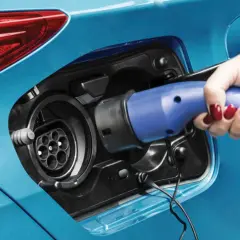 Dłoń z czerwonym lakierem na paznokciach podłącza ładowarkę do samochodu plug-in hybryda.