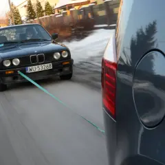 Czarny BMW holowany przez inny samochód, bo zabrakło paliwa. Co zamiast plaka do odpalenia? Lina holownicza!