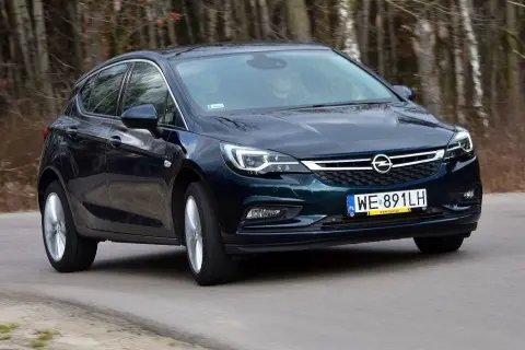 Ciemnozielona Astra K 1.6 CDTI w ruchu, z widocznym kierowcą za kierownicą, na tle lasu.