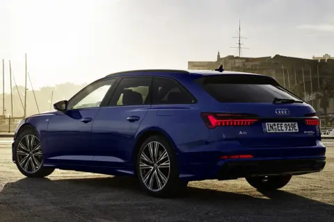 Niebieskie Audi A6 Avant z napisem "50 TFSI e" na klapie bagażnika, zaparkowane przy nabrzeżu z widokiem na zabytkową fortecę i żaglówki.