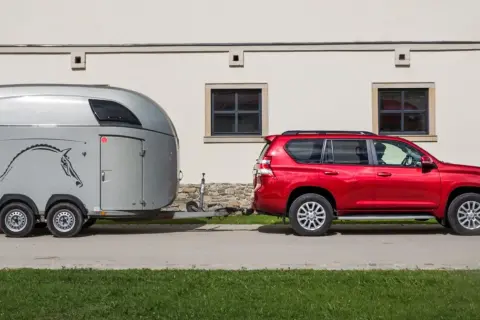 Czerwony SUV holuje przyczepę z koniem. B+E co daje? Możliwość przewiezienia ukochanego zwierzęcia w komfortowych warunkach.
