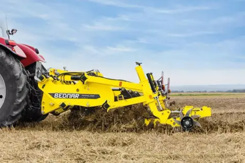 Czerwony traktor z żółtym agregatem uprawowym Bednar Terraland pracuje na polu.