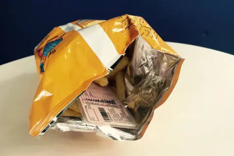 Otwarta paczka chipsów, a w środku etykieta z danymi, jakby to było **prawo jazdy w chipsach**.