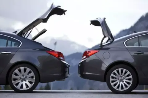 Dwa ciemnoszare sedany z otwartymi bagażnikami, przypominające kształtem hatchback. Góry w tle.
