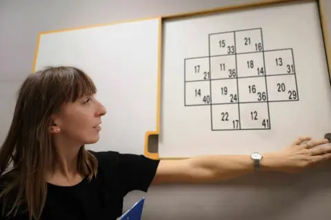 Kobieta podczas testów psychologicznych dla kierowców, wskazująca na tablicę z liczbami.