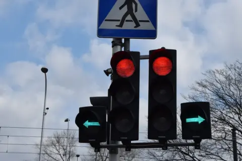 Sygnalizacja świetlna: czerwone światła dla jazdy prosto, zielona strzałka w lewo. Czy na strzałce w lewo można zawracać? Znak przejścia dla pieszych.