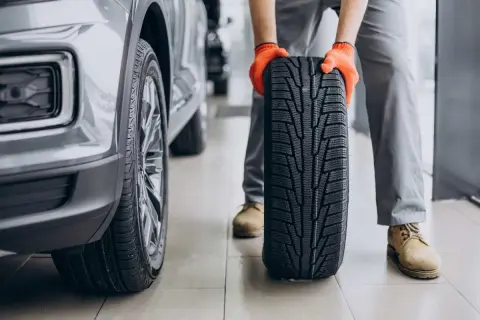 Mechanik w pomarańczowych rękawiczkach trzyma nowe opony letnie obok samochodu. Czas na test opon letnich!