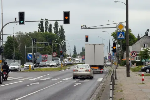 Kierowca srebrnego sedana decyduje się na przejazd na żółtym świetle, mimo że sygnalizator obok świeci na czerwono.
