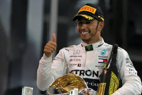 Lewis Hamilton, jeden z najlepsi kierowcy f1, świętuje zwycięstwo z pucharem i szampanem, pokazując kciuk w górę.