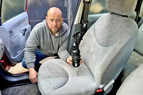 Mężczyzna z butelką środka do mycia tapicerki samochodowej przygotowuje się do odświeżenia wnętrza auta.