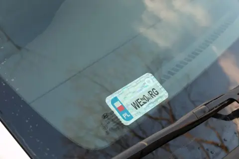 Naklejki na samochód, w tym obowiązkowe naklejki z numerem rejestracyjnym, umieszczone na przedniej szybie.