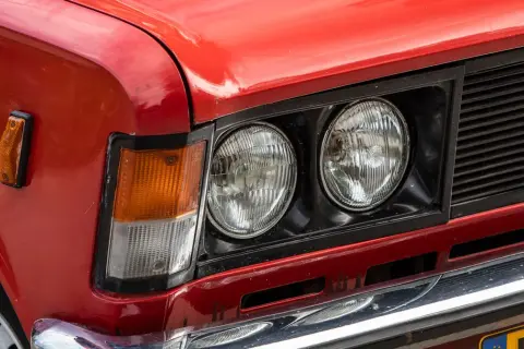 Czerwone auto z włoch, z podwójnymi okrągłymi reflektorami i pomarańczowym kierunkowskazem.