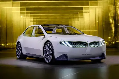 Biały koncept BMW Neue Klasse z futurystycznymi światłami i żółtym wnętrzem, prezentowany na tle złotej, lśniącej ściany.