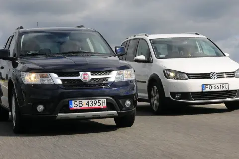 Dwa duże samochody rodzinne, ciemny Fiat i biały Volkswagen, jadą obok siebie po drodze.