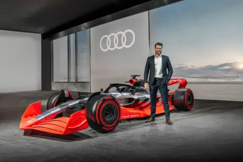 Mężczyzna w garniturze obok futurystycznego bolidu Audi F1 2026.